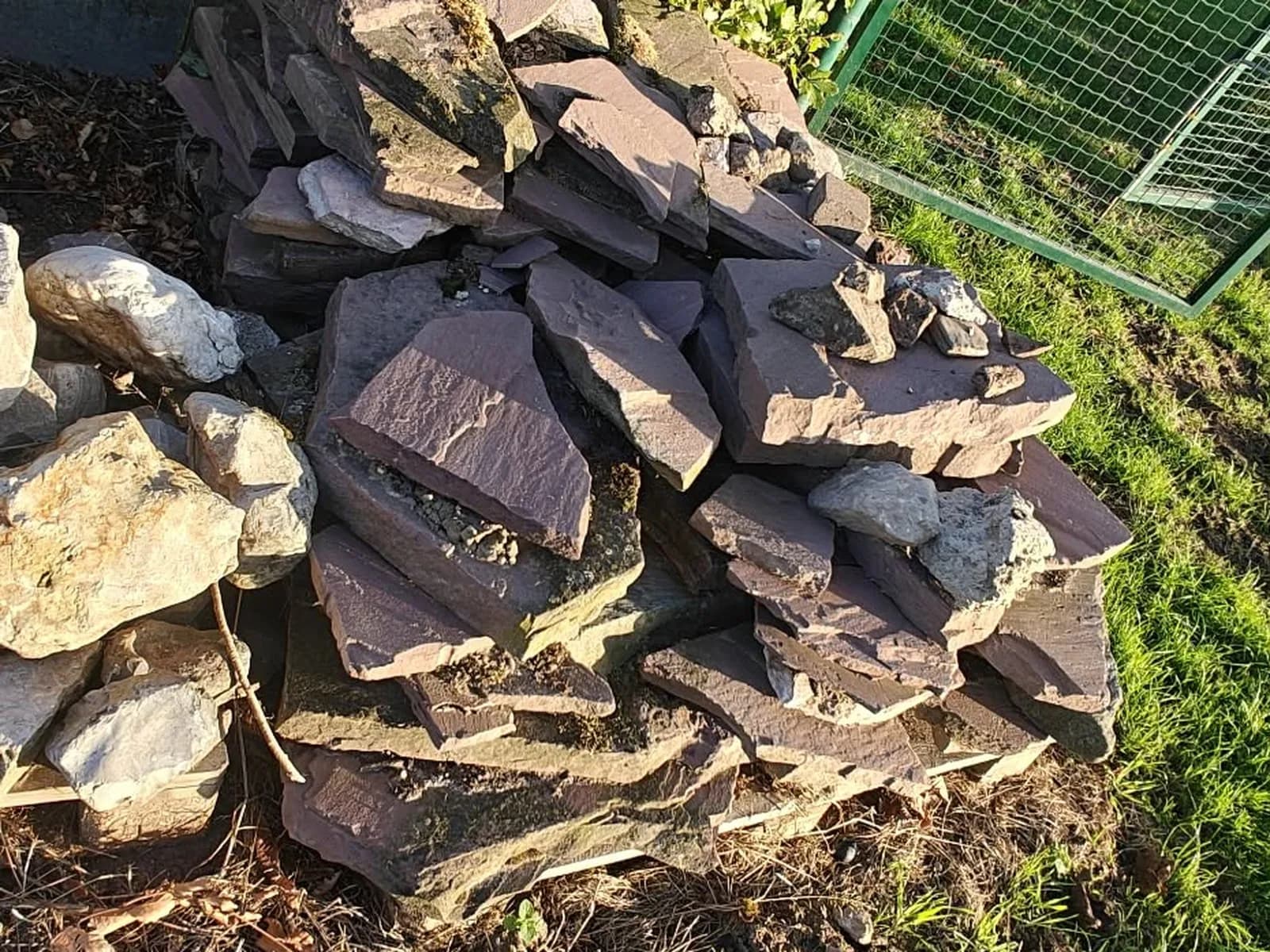 Natuursteen en rotsblokken gestapeld naast een haag, gesorteerd voor hergebruik en afvoer