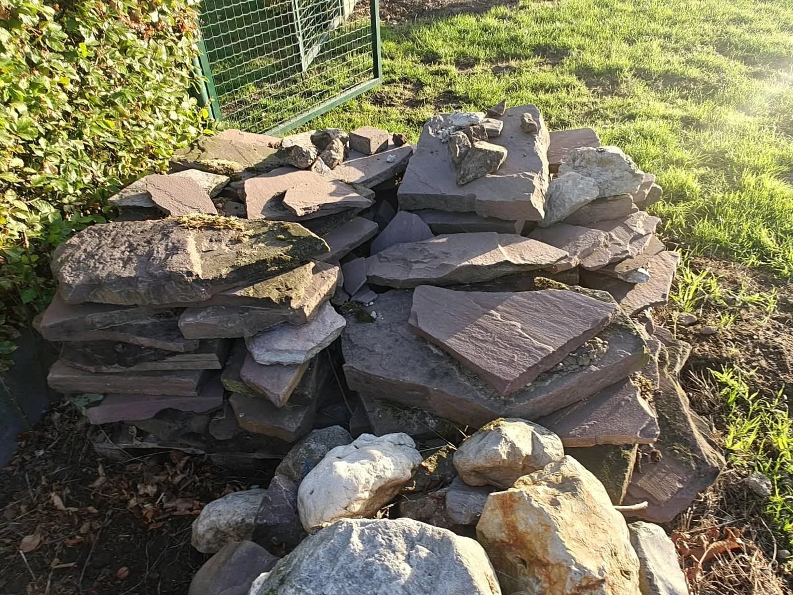 Stapel natuurstenen platen en rotsblokken in een tuinhoek, klaar om afgevoerd te worden