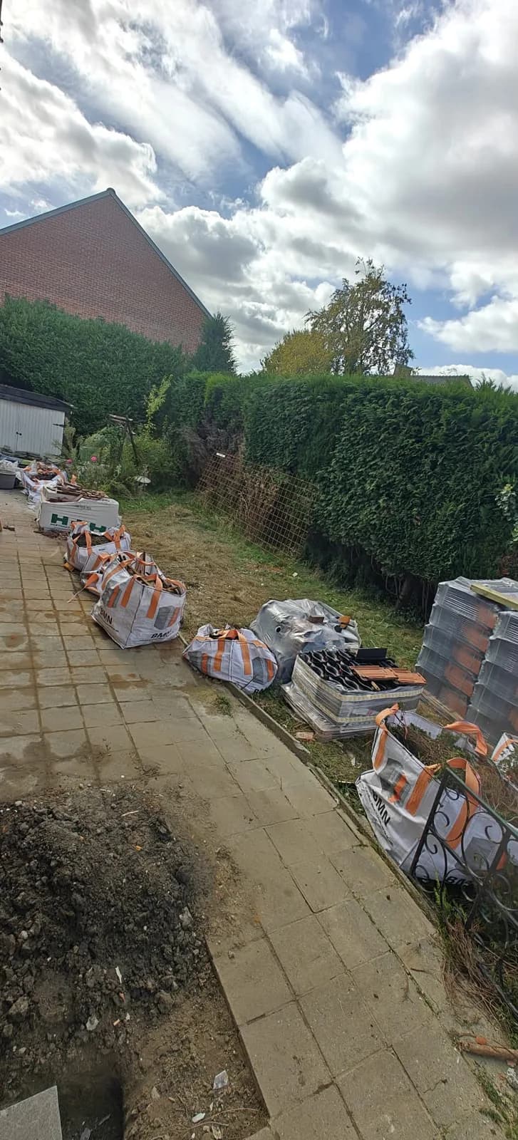 Terras en zijpad vol big bags met sloopafval en losse dakpannen, voor de afvoer